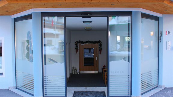 The entrance to a modern building with large glass windows. The area is clean and inviting, with a wooden-paneled ceiling. - Haus Martinshof - Obergurgl 