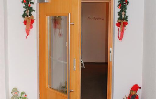 An open door with a festive decoration of pine branches and red bows. Next to the door stand two Christmas figures and a small statue. - Haus Martinshof - Obergurgl 