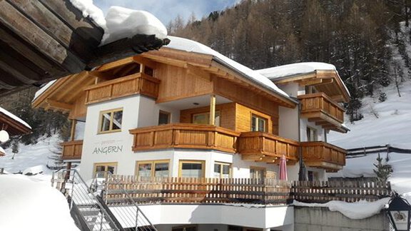 A modern chalet in the snow with wood cladding and balconies. Surrounded by snow-covered trees and mountains. - Pension Angern - Obergurgl 