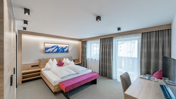 A modern bedroom with a double bed and wooden-paneled walls. The room is bright and cozy, with windows and a desk. - Pension Broser - Obergurgl 