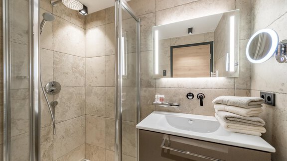 A modern bathroom with a shower and a sink. There are bright tiles and fresh towels. - Pension Broser - Obergurgl 