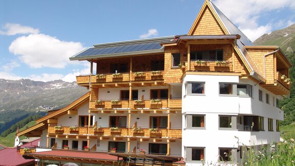 A charming hotel in alpine style with wooden paneling and balconies. The surroundings offer a picturesque mountain landscape and blue skies. - Schönblick Gurgl - Obergurgl 