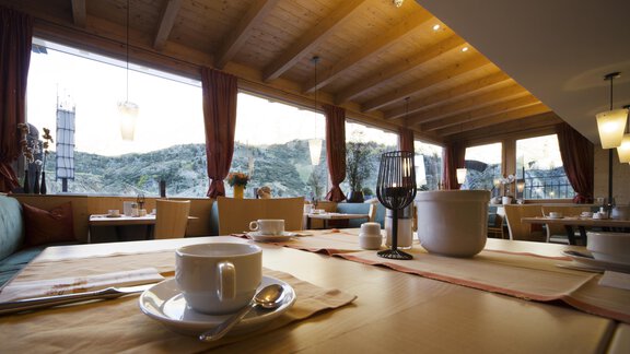 A cozy restaurant with a wooden ceiling and large windows. The view shows gentle hills and a pleasant atmosphere. - Schönblick Gurgl - Obergurgl 