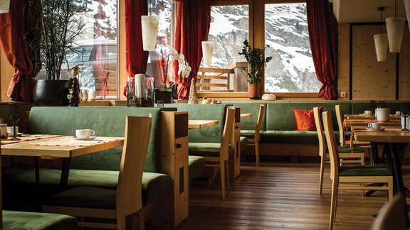 A cozy restaurant with wooden tables and green benches. Large windows offer a view of the snowy landscape. - Schönblick Gurgl - Obergurgl 