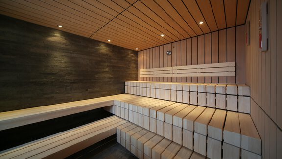 A modern sauna interior with clear wooden surfaces and tiered benches. Soft lighting creates a relaxing atmosphere. - Schönblick Gurgl - Obergurgl 