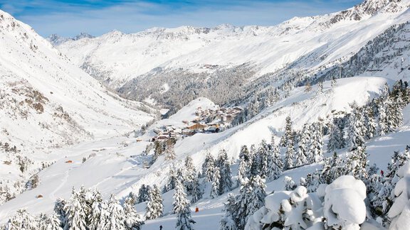 A winter mountain landscape with snow-covered hills and trees. In the background, the snow-covered peaks and a small village can be seen. - Villa Michelle - Obergurgl 
