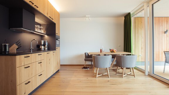 A modern kitchen with wooden furniture and a cozy dining area.  
Large windows provide plenty of light and a friendly atmosphere. - All-Suite Resort Ötztal - Oetz