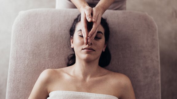 Eine Frau erhält eine Gesichtsmassage auf einer Liege. Sie sieht entspannt aus und trägt ein Handtuch. - Hotel habicher hof - Oetz