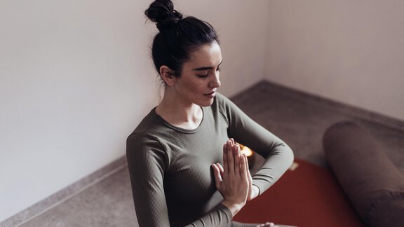 Eine Frau sitzt im Yoga-Stil mit gefalteten Händen. Sie wirkt entspannt in einem neutralen Raum. - Hotel habicher hof - Oetz