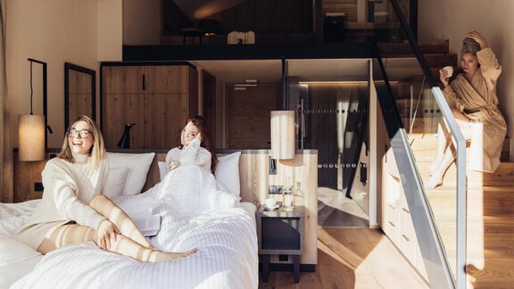Ein modernes Zimmer mit hellen Holzdetails und einer Treppe. Drei Frauen entspannen im Bett und genießen die gemütliche Atmosphäre. - Hotel habicher hof - Oetz