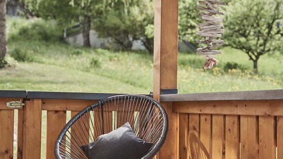 Ein stilvoller Sessel steht auf einer Veranda, umgeben von einem Holzgitter. Im Hintergrund sieht man eine grüne Landschaft mit Bäumen. - Adventure Paradise - Sautens