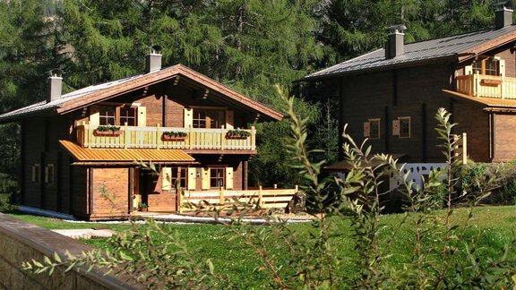 Two cozy wooden houses surrounded by trees. The garden is green and inviting. - Almdorf Waldesruh - Sölden