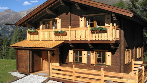 A traditional wooden house in the mountains, surrounded by beautiful landscapes. The balconies are adorned with flower boxes and the atmosphere conveys coziness. - Almdorf Waldesruh - Sölden