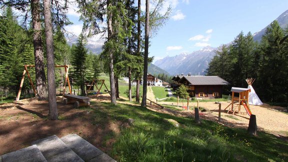 A beautiful playground surrounded by trees in the mountains. In the background, huts and a tent can be seen. - Almdorf Waldesruh - Sölden