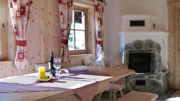 A cozy dining area with wooden furniture and a fireplace. The walls are made of wood, and the windows are adorned with decorative curtains. - Almdorf Waldesruh - Sölden