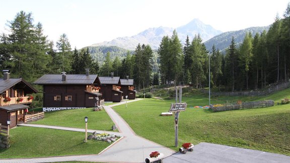 A picturesque Alpine landscape with wooden huts and green meadows. In the background, high mountains rise under a clear sky. - Almdorf Waldesruh - Sölden