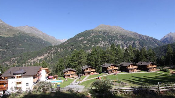 A picturesque mountain landscape with several chalets and green meadows. In the background, tall mountains and a clear sky can be seen. - Almdorf Waldesruh - Sölden