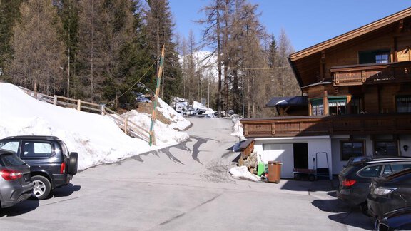 A quiet parking lot with several cars and snow-covered areas. In the background, there are trees and a clear sky. - Almdorf Waldesruh - Sölden