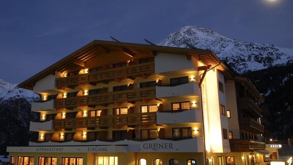 A cozy hotel with illuminated balconies amidst a mountainous landscape. The sky is clear and the moon shines at night. - Alpengasthof Grüner - Sölden
