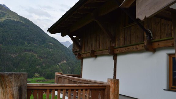 A traditional wooden house with a balcony and a view of the mountains. The surroundings are green and mountainous. - Am Trogwohl - Sölden