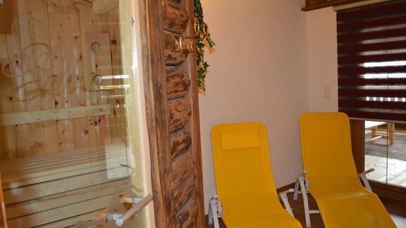 A cozy sauna area with two yellow loungers and a wooden-paneled sauna. The room exudes relaxation and a wellness atmosphere. - Am Trogwohl - Sölden