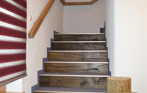 A staircase with wooden steps and blue carpet covering. On the wall, red blinds and a window can be seen. - Am Trogwohl - Sölden
