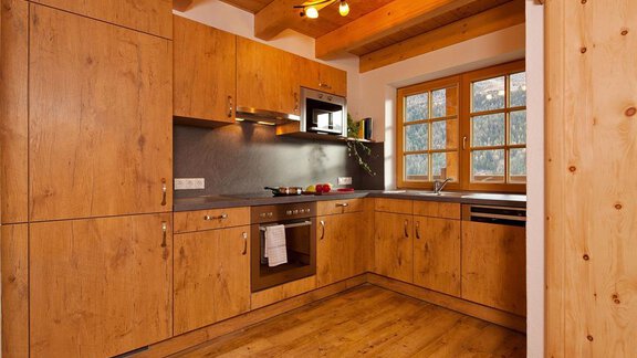 A modern kitchen with wooden cabinets and a stone countertop.  
Plenty of natural light from the window creates a warm atmosphere. - Andis Almdorf - Sölden