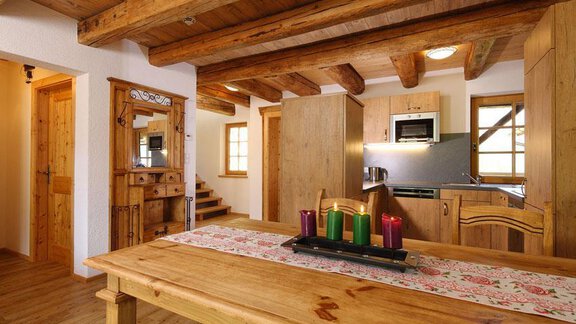 A cozy living space with wooden furniture and a modern kitchen. The table is beautifully decorated with candles and a tablecloth. - Andis Almdorf - Sölden