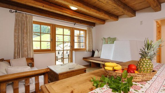 A cozy living space with wooden furniture and large windows. On the table, there is a fruit bowl with various fruits. - Andis Almdorf - Sölden