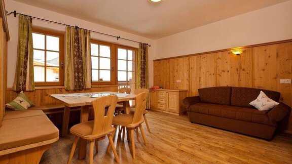 A cozy living space with wooden furniture and a dining area. Large windows let in a lot of light and create a warm atmosphere. - Andis Almdorf - Sölden