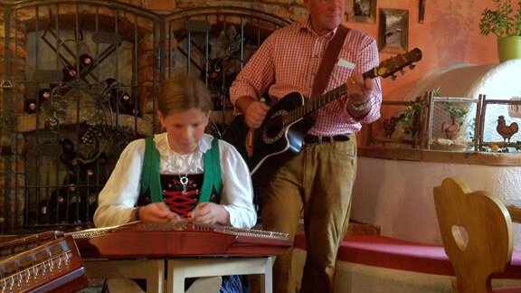 Ein gemütliches Restaurant mit traditioneller bayerischer Musik. Eine Frau spielt ein Instrument, während ein Mann mit einer Gitarre singt. - Andis Almdorf - Sölden