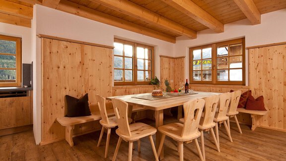 A cozy dining area with a large wooden table and chairs made of light wood. The walls and ceiling are also made of wood, creating a warm atmosphere. - Andis Almdorf - Sölden