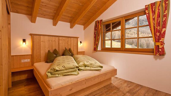 A cozy bedroom with wooden plank floors and a large window front. The bedding is green, and the walls are in warm wood tones. - Andis Almdorf - Sölden
