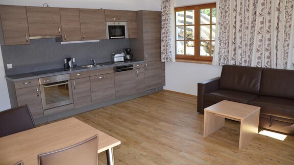 A modern kitchen with wooden cabinets and a cozy living room. The space is bright and welcoming with a dining table and a couch. - Andis Almdorf - Sölden
