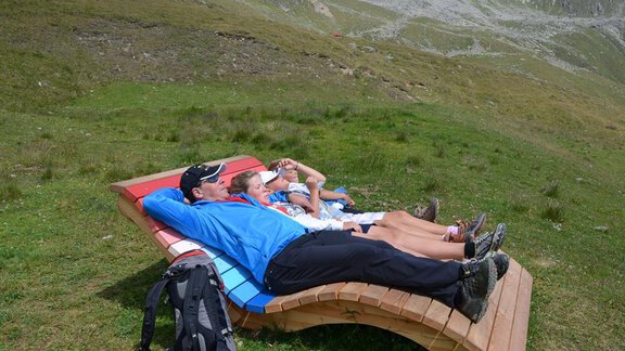 Three people are relaxing on loungers in a green mountain landscape. The surroundings are quiet and picturesque, surrounded by mountains. - Andis Almdorf - Sölden