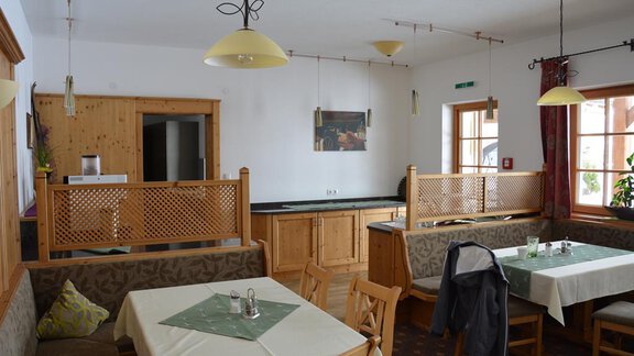A cozy dining area with wooden furniture and tables. The walls are light and there are large windows that provide plenty of light. - Andis Almdorf - Sölden
