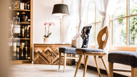 A stylish room with two wooden chairs and a large window. In the background, a decorative display case and plants can be seen. - Andre Arnold - Boutique Hotel - Sölden