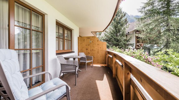 A cozy balcony with two chairs and a table. In the background, green trees can be seen that create a serene atmosphere. - Andre Arnold - Boutique Hotel - Sölden