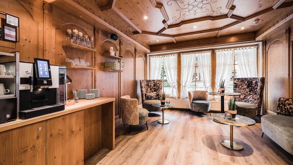 A cozy room with wood paneling and elegant furniture. Beverages are on the wall and there is a comfortable seating area with windows. - Andre Arnold - Boutique Hotel - Sölden