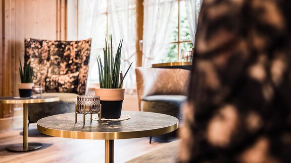 A stylish room with modern furniture and large windows. A plant in a pot is on a round table, surrounded by cozy armchairs. - Andre Arnold - Boutique Hotel - Sölden