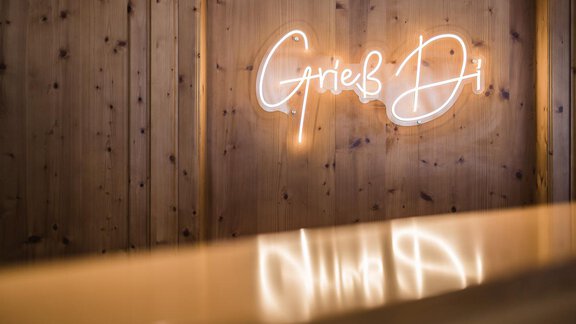 A cozy room with a wooden wall and a glowing neon sign. The words "Grieß Di" are friendly and inviting. - Andre Arnold - Boutique Hotel - Sölden