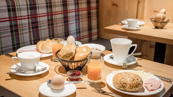 A hearty breakfast with rolls, boiled eggs, and various drinks. The tables are made of wood and decorated with a cozy atmosphere. - Apart Garni Enzian - Sölden