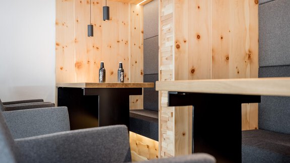 A modern room with wooden walls and simple tables. There are gray seating areas and some bottles on the tables. - Apart Garni Enzian - Sölden