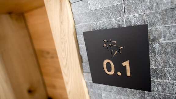A numbered sign with the inscription "0.1" is attached to a wall made of grey stones. The area has a modern and stylish design. - Apart Garni Enzian - Sölden
