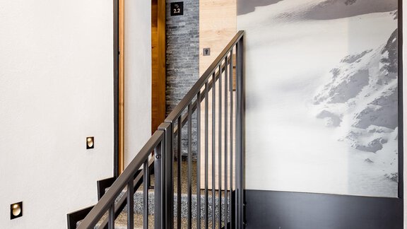 A modern staircase with a metal railing. A mountain picture is visible on the wall, creating a calm atmosphere. - Apart Garni Enzian - Sölden