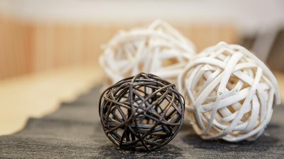 A stylish table decoration with three decorative balls made of rattan. Two are white and one is black, placed on a dark gray table runner. - Apart Garni Enzian - Sölden