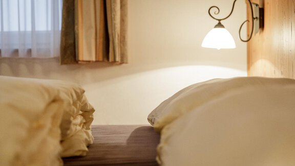 A cozy bedroom with two pillows and soft lighting. The curtains are light and create a pleasant atmosphere. - Apart Garni Enzian - Sölden