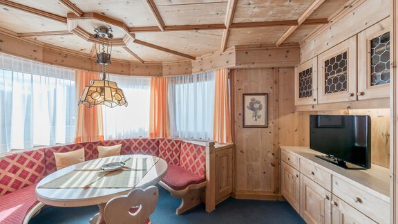 A cozy room with wooden walls and an inviting seating area. A round table is in the center, surrounded by red cushions and a television on the wall. - Apart Hotel Garni Wieser - Sölden