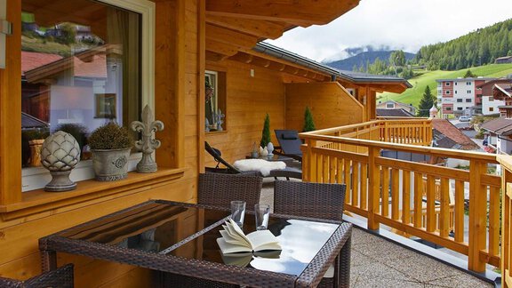 Ein gemütlicher Balkon mit einem Tisch und Stühlen aus Rattan. Im Hintergrund sind die Berge und ein Teil der Stadt sichtbar. - Alpen Diamond Top 100 | 300 | 700 - Sölden