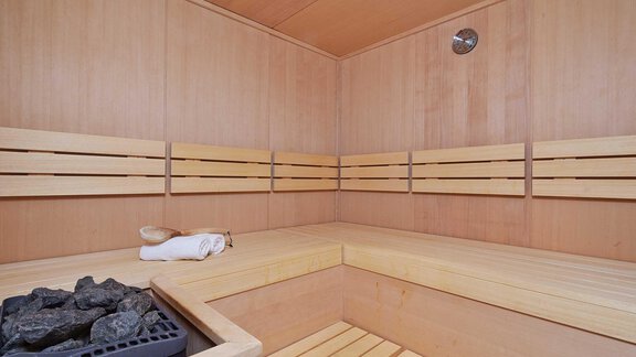 Eine gemütliche Sauna mit Holzbänken und einem Steingitter. Handtuch und Saunaofen sind gut sichtbar. - Alpen Diamond Top 100 | 300 | 700 - Sölden